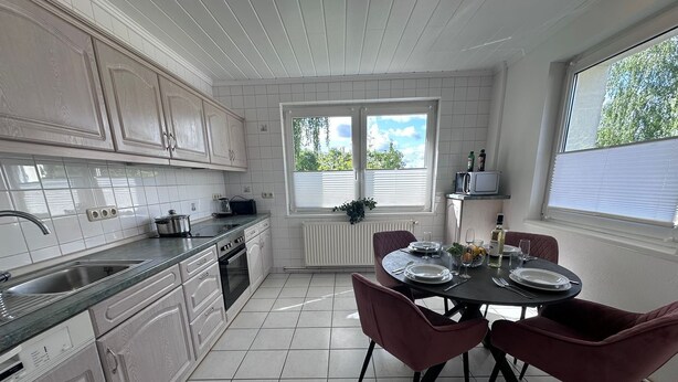 A modern kitchen with white cabinetry, a dining table set for four, and a view of greenery outside.