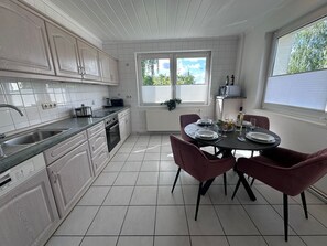 A modern kitchen with white cabinetry, a dining table set for four, and a view of greenery outside. - Eickhof Vacation Home with a fireplace, pool table, ping-pong table, foosball table, and free Wi-Fi - (Warnow)