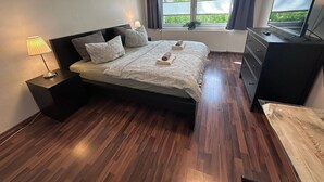 A bedroom with a bed, bedside lamps, a dresser, a television, and a window with curtains.