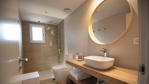 Ein modernes Badezimmer mit einem großen runden Spiegel, einem Holzwaschtisch, einem weißen Waschbecken und einer Duschkabine aus Glas.