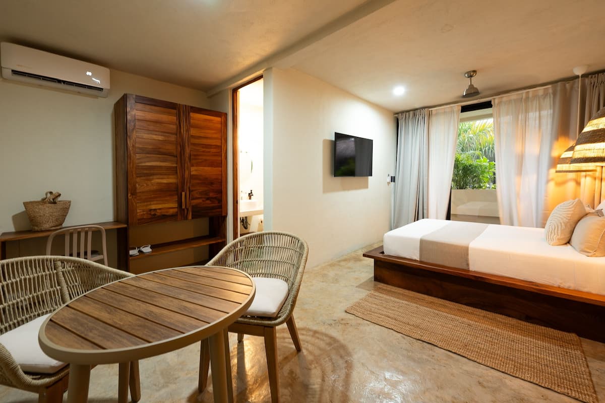 A room with a bed, a TV, wicker furniture, and a table.