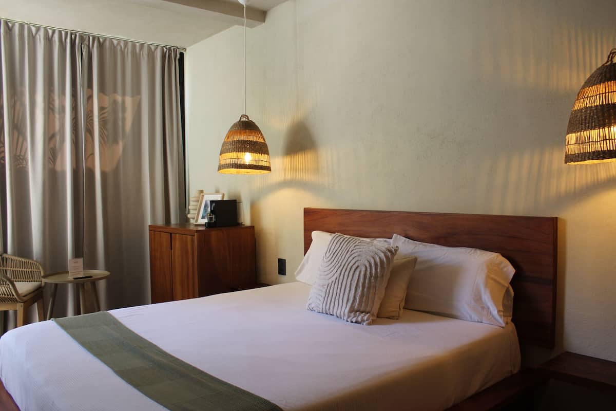 A hotel room with a large bed, two hanging lamps, a wooden headboard, a nightstand, a chair, and a desk.