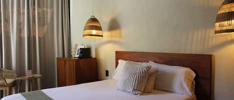 Een hotelkamer met een groot bed, twee hanglampen, een houten hoofdbord, een nachtkastje, een stoel en een bureau.