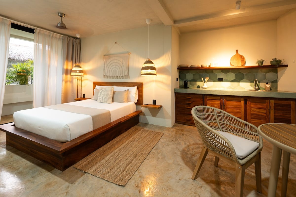 A bedroom with a wooden bed, bedside lamps, a nightstand, a wicker chair, and a small table.