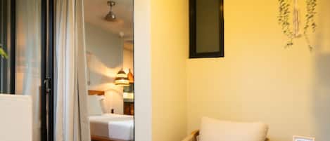 A hotel room with a bed, a chair, a small table, and a hanging plant.