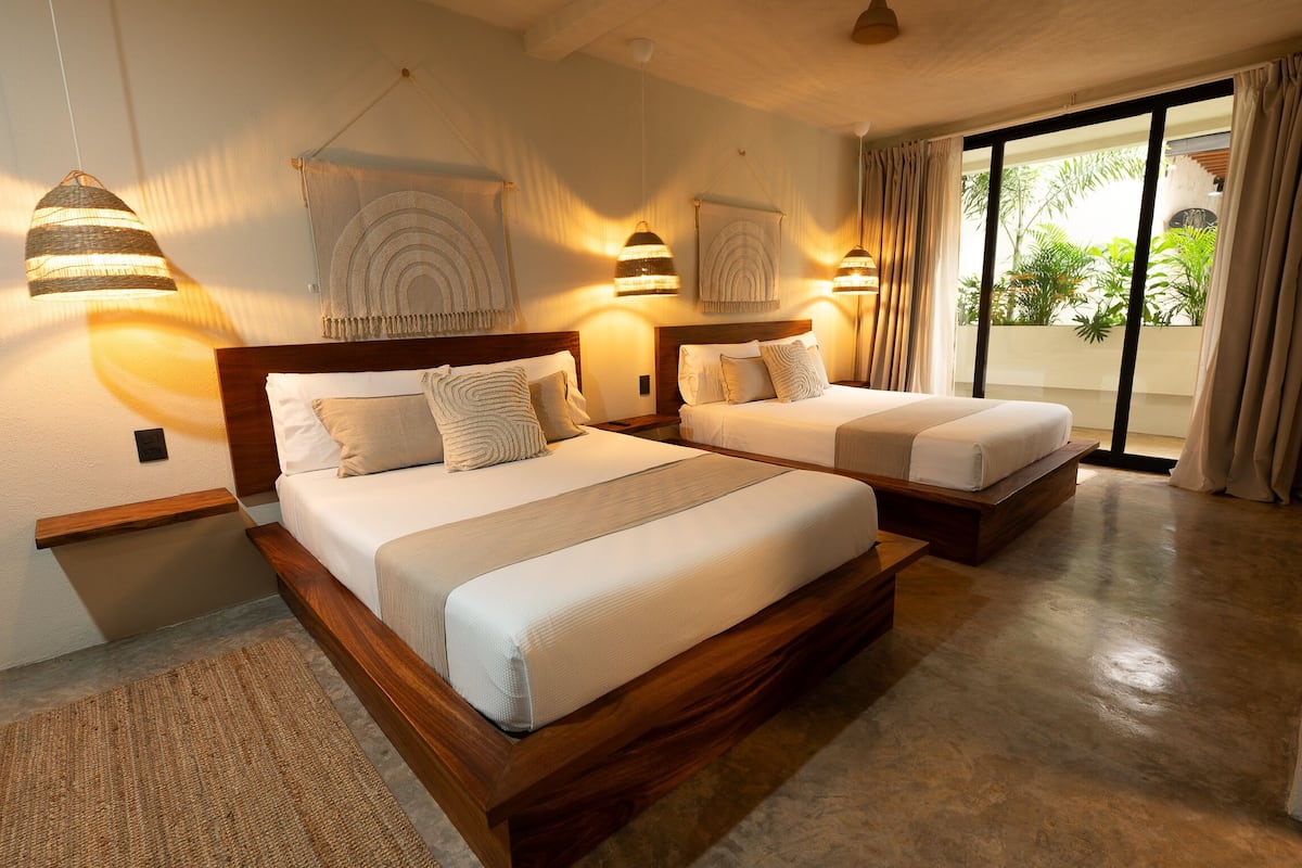 A hotel room with two beds, a large window with curtains, and wall-mounted lamps.