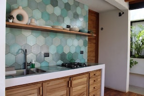Una cocina con salpicadero de azulejos hexagonales, armarios de madera, un lavamanos de acero inoxidable y una estufa a gas.