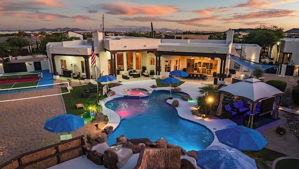 Zona de piscina con hidromasaje, sombrillas y vista a un paisaje urbano al atardecer.