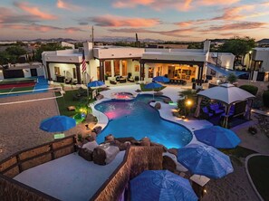 A pool area with a hot tub, umbrellas, and a view of a cityscape at dusk. - Private Oasis, Pickleball, Sand Volleyball, Sleeps 24 (Phoenix)