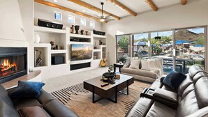 Una sala de estar moderna con chimenea, un televisor grande y vistas a una zona de piscina exterior.