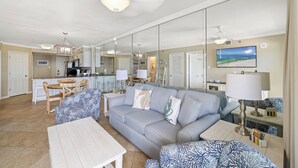A spacious living room with a grey sofa, a coffee table, and a dining area with a table and chairs. - Tradewinds 605 by Liquid Life (Orange Beach)