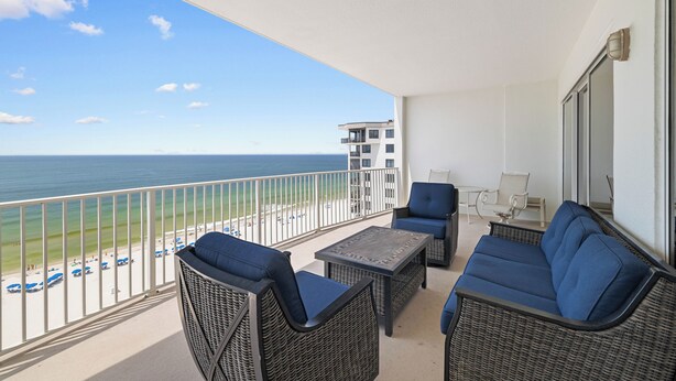 A balcony with wicker furniture, a view of the beach, and a building in the background. - Regency Isle 1010 by Liquid Life (Orange Beach)