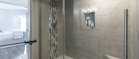 A modern bathroom with a glass-enclosed shower, a tiled floor, and a small mirror on the wall.