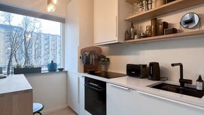 Une cuisine moderne avec des meubles blancs, un lave-vaisselle encastré, une cuisinière noire et une fenêtre donnant sur un paysage urbain.