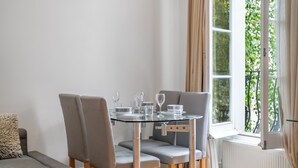 A dining area with a glass table, grey upholstered chairs, and a window with curtains. - Contemporary 1B apartment - Paddington St (Greater London)