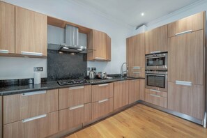 Eine moderne Küche mit Holzausbau, einem Gasherd, einer Dunstabzugshaube und eingebauten Backöfen.