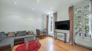 A modern living room with a sofa, TV, dining table, and large windows. - Contemporary 1B apartment - Paddington St (Greater London)