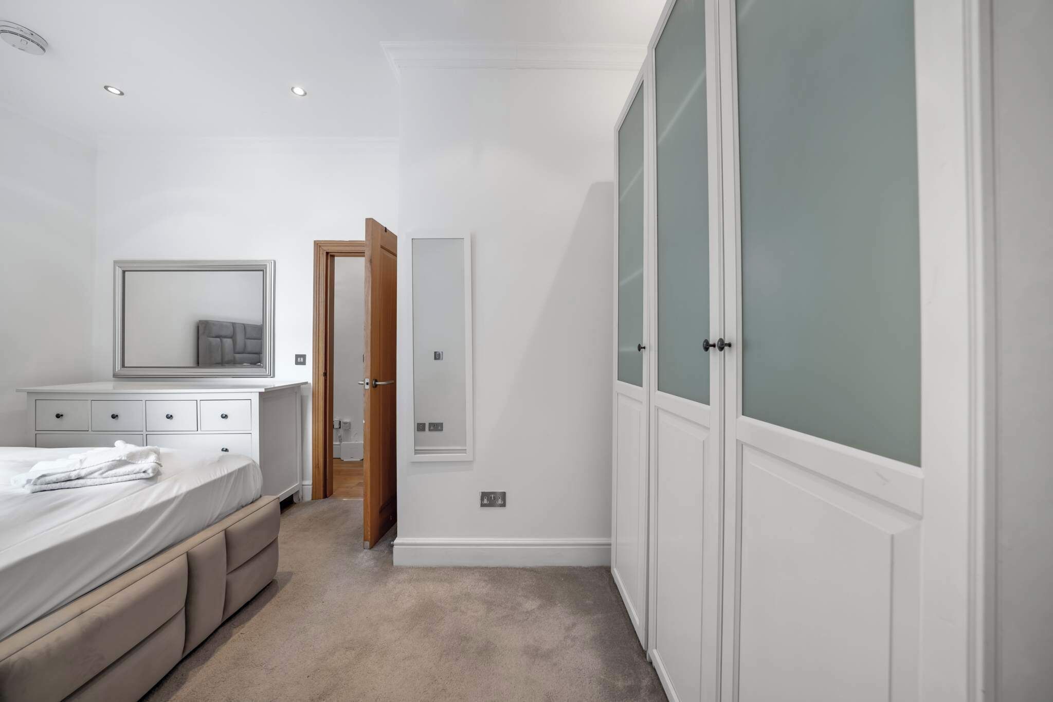 Un dormitorio con cama, cómoda, espejo, armario y una puerta que da a otra habitación.