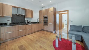 A modern kitchen with wooden cabinets, stainless steel appliances, and a glass coffee table. - Contemporary 1B apartment - Paddington St (Greater London)