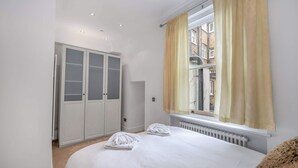 A bedroom with a bed, a wardrobe, a window with curtains, and a radiator. - Contemporary 1B apartment - Paddington St (Greater London)