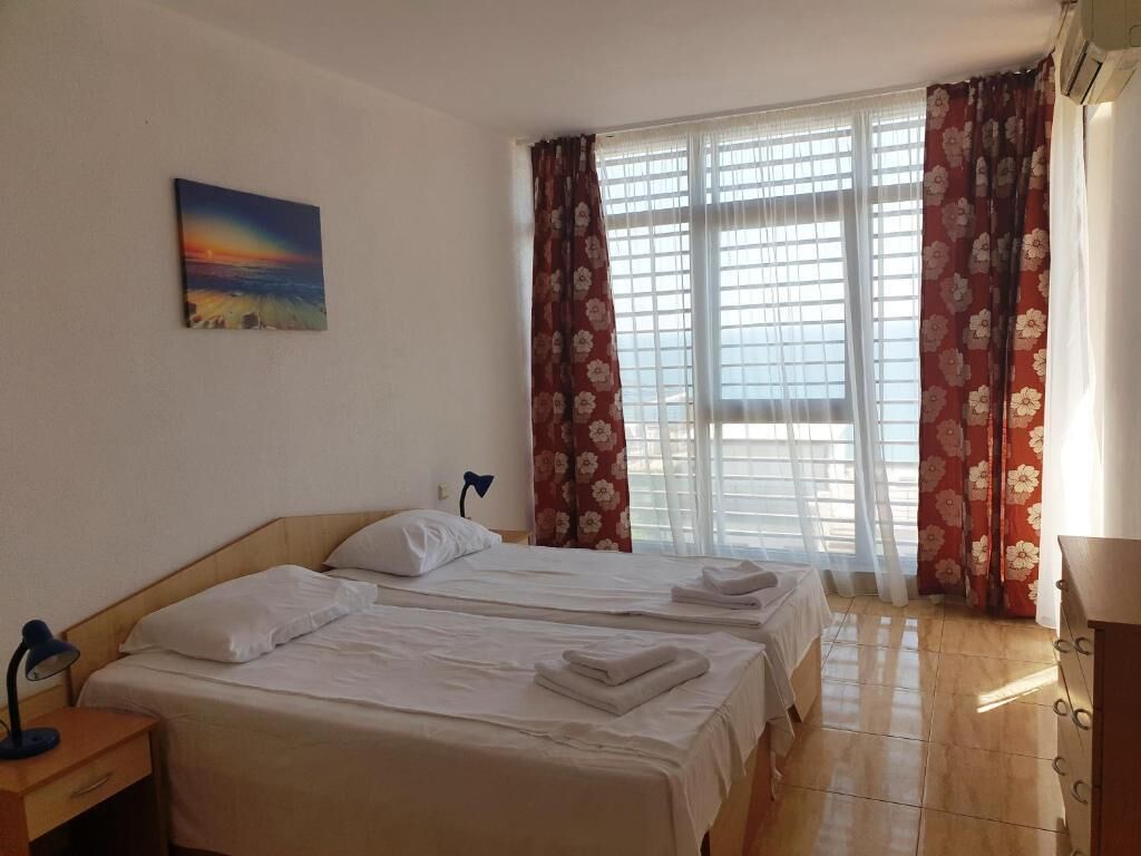 A hotel room with two beds, a painting on the wall, and a window with curtains.