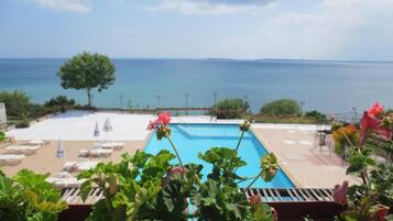 A pool area with lounge chairs and a view of the sea.