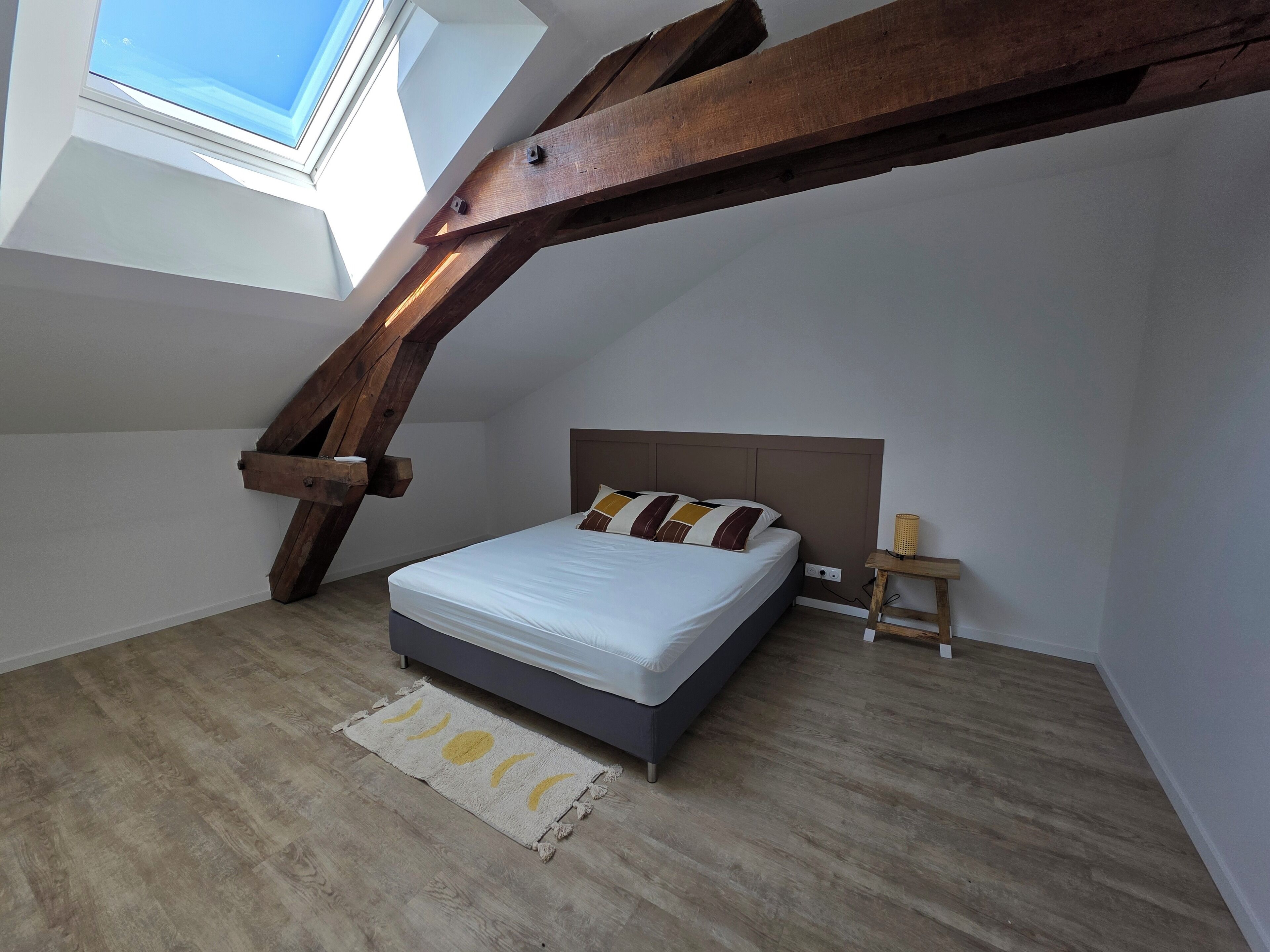 Ein Schlafzimmer mit schrägem Dach, einem Bett, einem Nachttisch und einer kleinen Lampe.