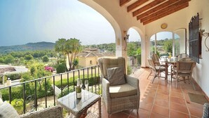 Ein Balkon mit Korbmöbeln, einem Tisch mit Flasche und Gläsern sowie Blick auf die Landschaft.
