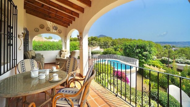 Ein Balkon mit einem für Tee gedecktem Tisch, mit Blick auf einen Pool und üppiges Grün.