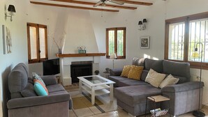 Ein Wohnzimmer mit zwei Sofas, einem Kamin, einem Deckenventilator und großen Fenstern.