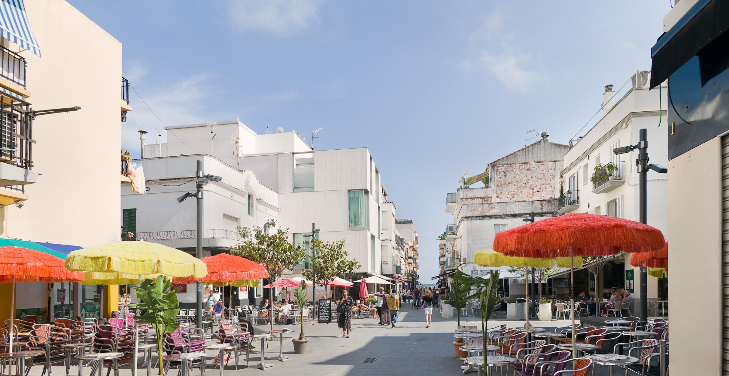 A street with outdoor seating, umbrellas, and buildings with balconies.