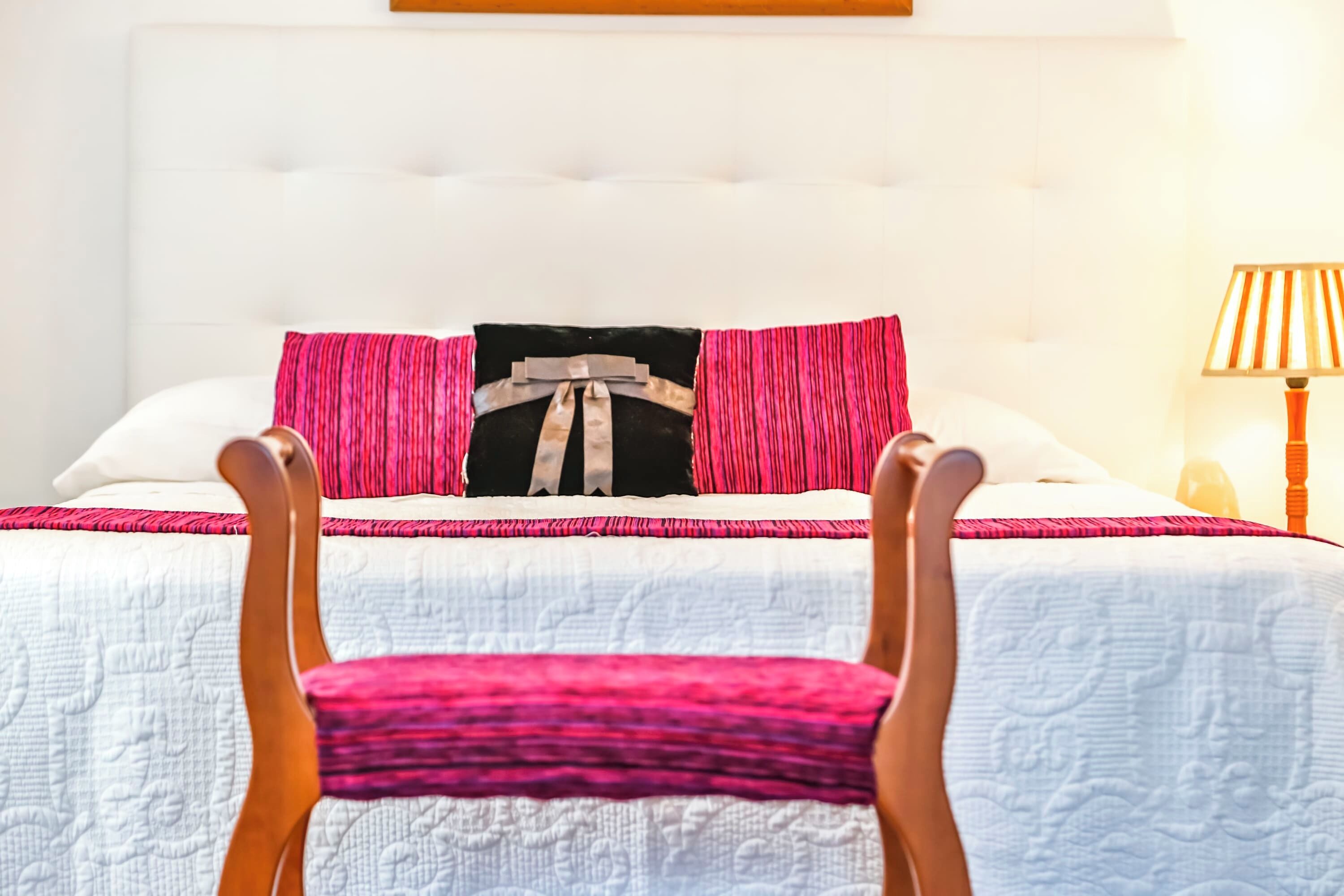A bed with a white headboard, pink and black pillows, and a wooden chair in front.