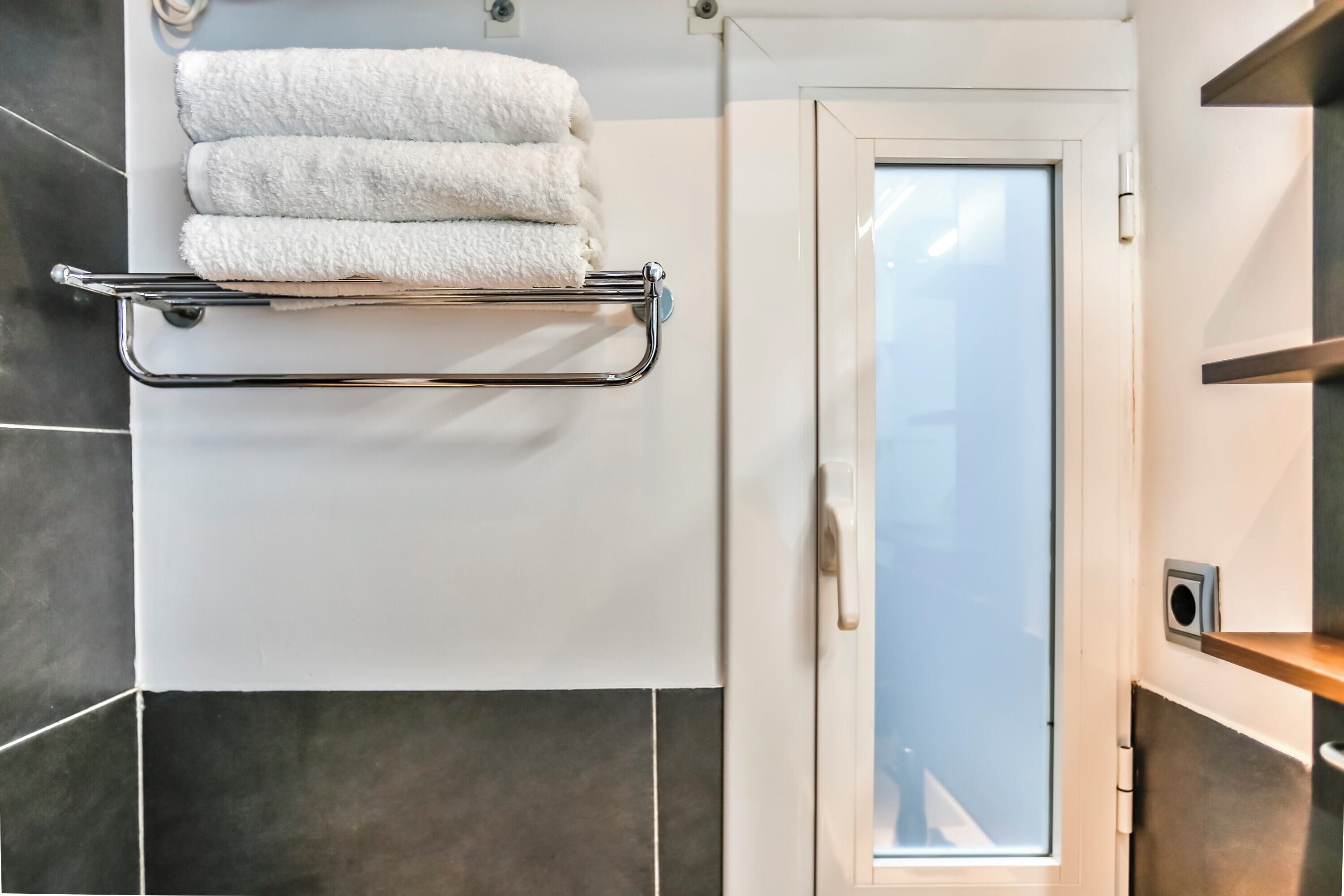 Une salle de bain avec un porte-serviettes sur lequel sont disposées trois serviettes blanches, une porte en verre et un espace douche.