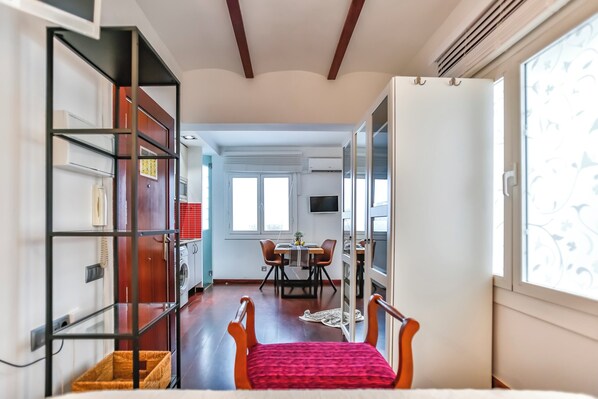 A modern kitchen with a dining area, a TV mounted above the table, and a large window providing natural light.
