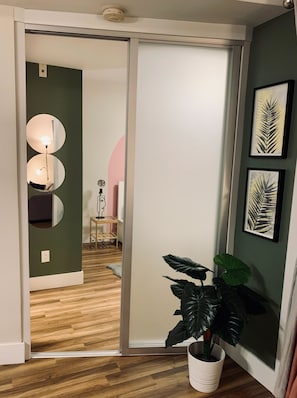 Ein modernes Interieur mit einer Schiebetür, die zu einem Raum führt, einem großen Spiegel, einem Blumentopf und gerahmten Kunstwerken an der Wand.