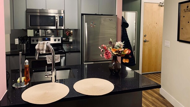 Cocina moderna con electrodomésticos de acero inoxidable, encimera negra y puerta de madera.