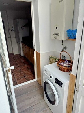 A laundry room with a washing machine, a small shelf with a basket, and a door leading to another room. - Casa Niebla        . (Vejer de la Frontera)