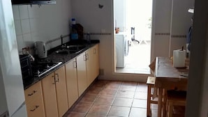 Une cuisine équipée d’une cuisinière, d’un évier et de placards, qui donne sur un coin repas avec une table et des chaises.