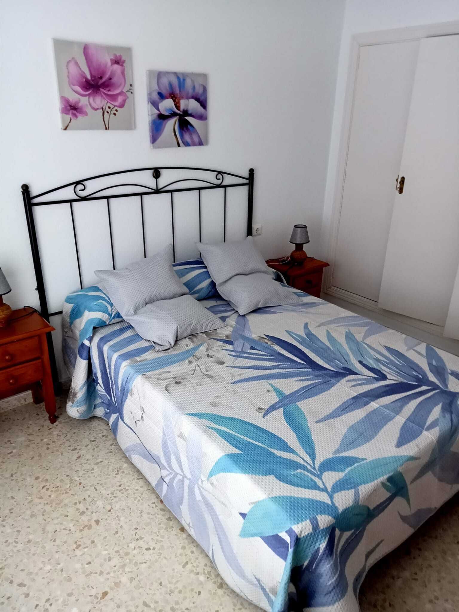 A bed with a floral bedspread, two pillows, a nightstand with a lamp, and a door in the background.