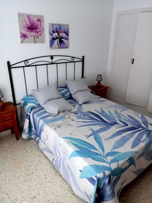 A bed with a floral bedspread, two pillows, a nightstand with a lamp, and a door in the background.