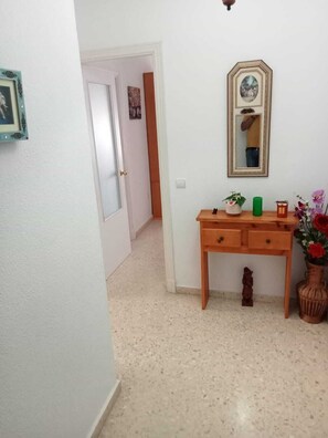 A hallway with a wooden desk, a mirror, and a vase with flowers.