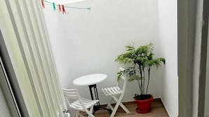 Un petit espace patio avec une table et des chaises blanches, une plante en pot et un fil à linge orné d’épingles à linge colorées.