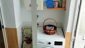 Un espace buanderie compact comprenant un lave-linge, une étagère avec des produits de nettoyage et un panier.