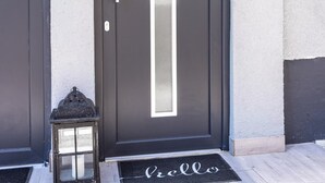 A modern building entrance with two dark-colored doors, a small lantern, and a 'hello' mat. - Premium Suite - Forest view - Balcony - Black Forest (Bühl)
