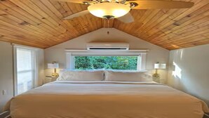 Een slaapkamer met een houten plafond, een groot bed, twee nachtkastjes en een raam met uitzicht op groen.