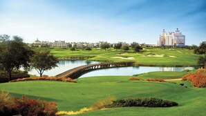 A golf course with a bridge over a pond, surrounded by greenery and buildings in the background. - Resort Townhome w/ Pool Access & Outdoor Retreat (Kissimmee)