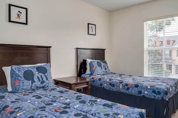 Ein Hotelzimmer mit zwei Betten, jeweils mit Mickey Mouse Bettwäsche, einem kleinen Nachttisch und einem Fenster mit Jalousien.