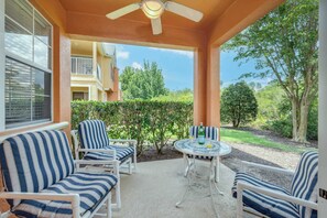 Eine überdachte Terrasse mit weißen Möbeln, einem runden Tisch und einem Deckenventilator.