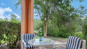 A patio with two striped chairs, a round table, a bottle of Pellegrino water, and glasses. - Resort Townhome w/ Pool Access & Outdoor Retreat (Kissimmee)