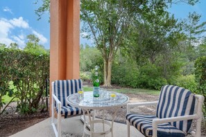 Une terrasse avec deux chaises à rayures, une table ronde, une bouteille d’eau Pellegrino et des verres.